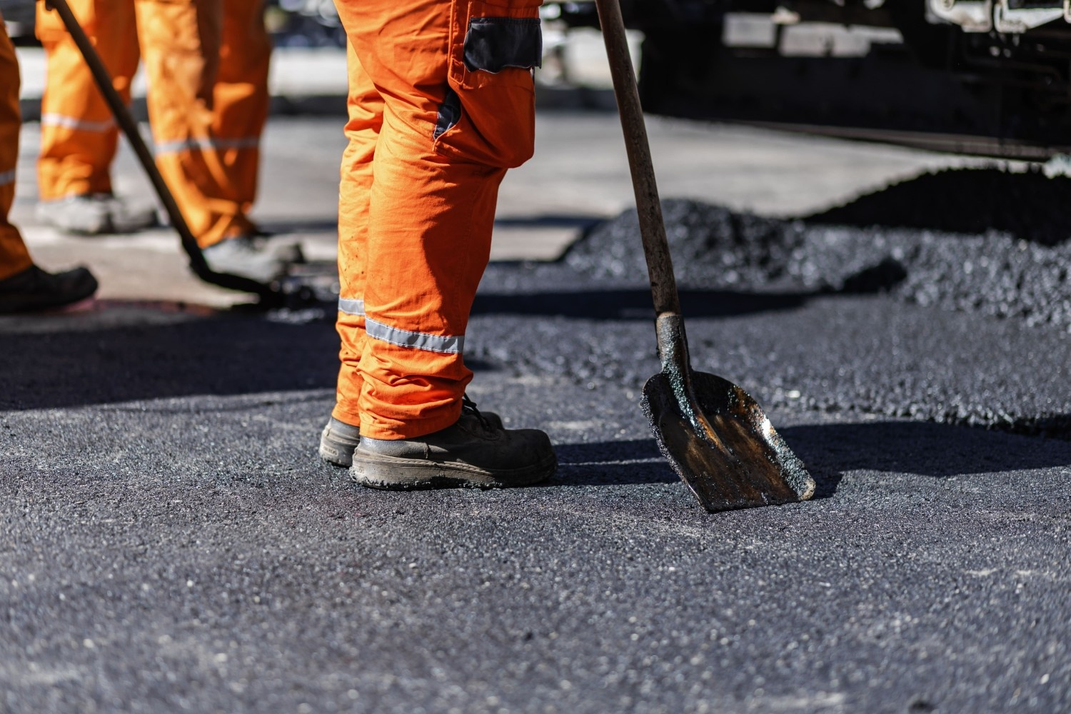 Construction workers using heavy equipment to lay fresh asphalt on a roadway during an asphalt paving project
